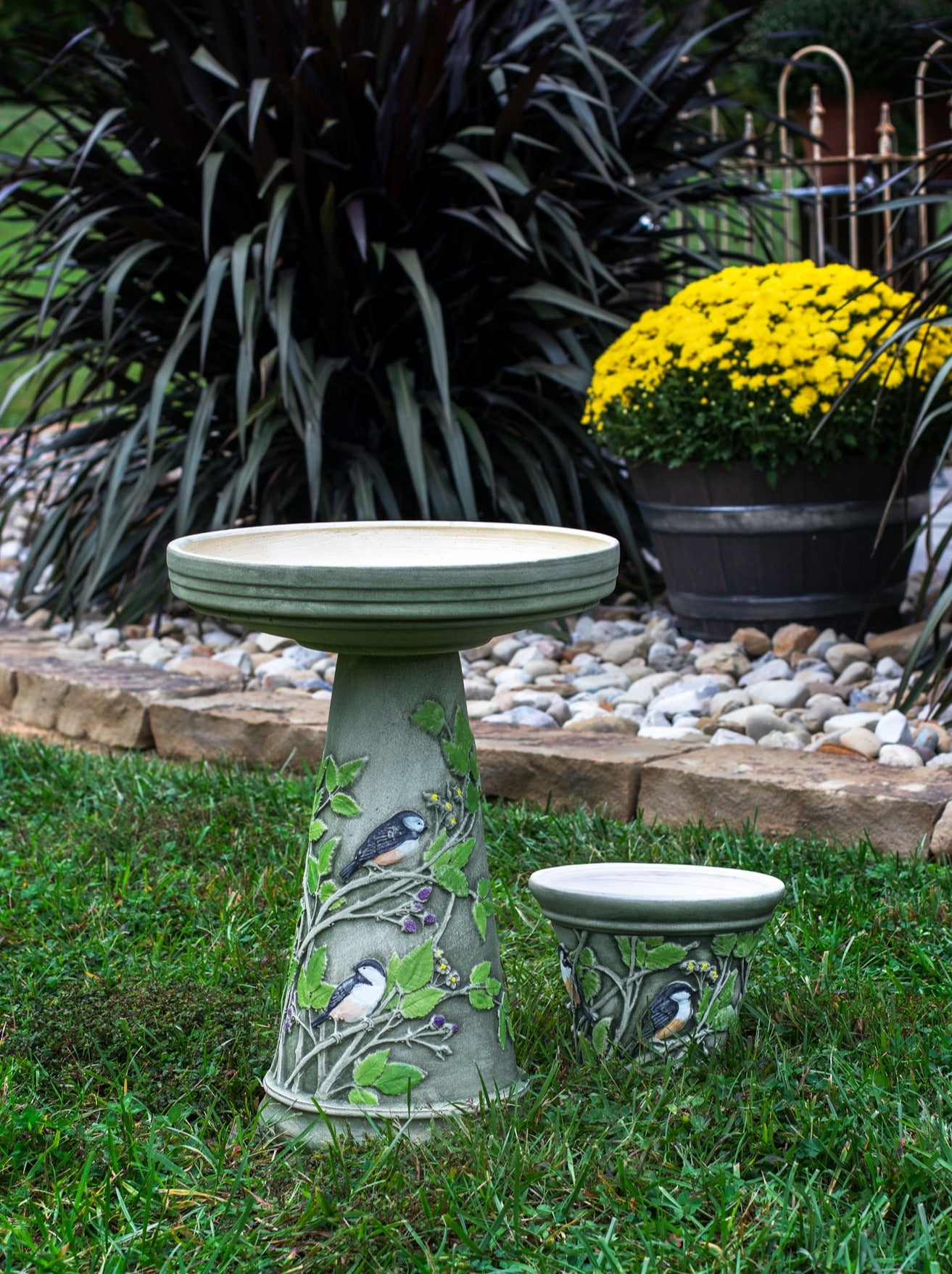 Hand painted ceramic birdbath set with chickadee birds green leaves and purple berries. Matching 10" planter next to it in a landscaped garden area