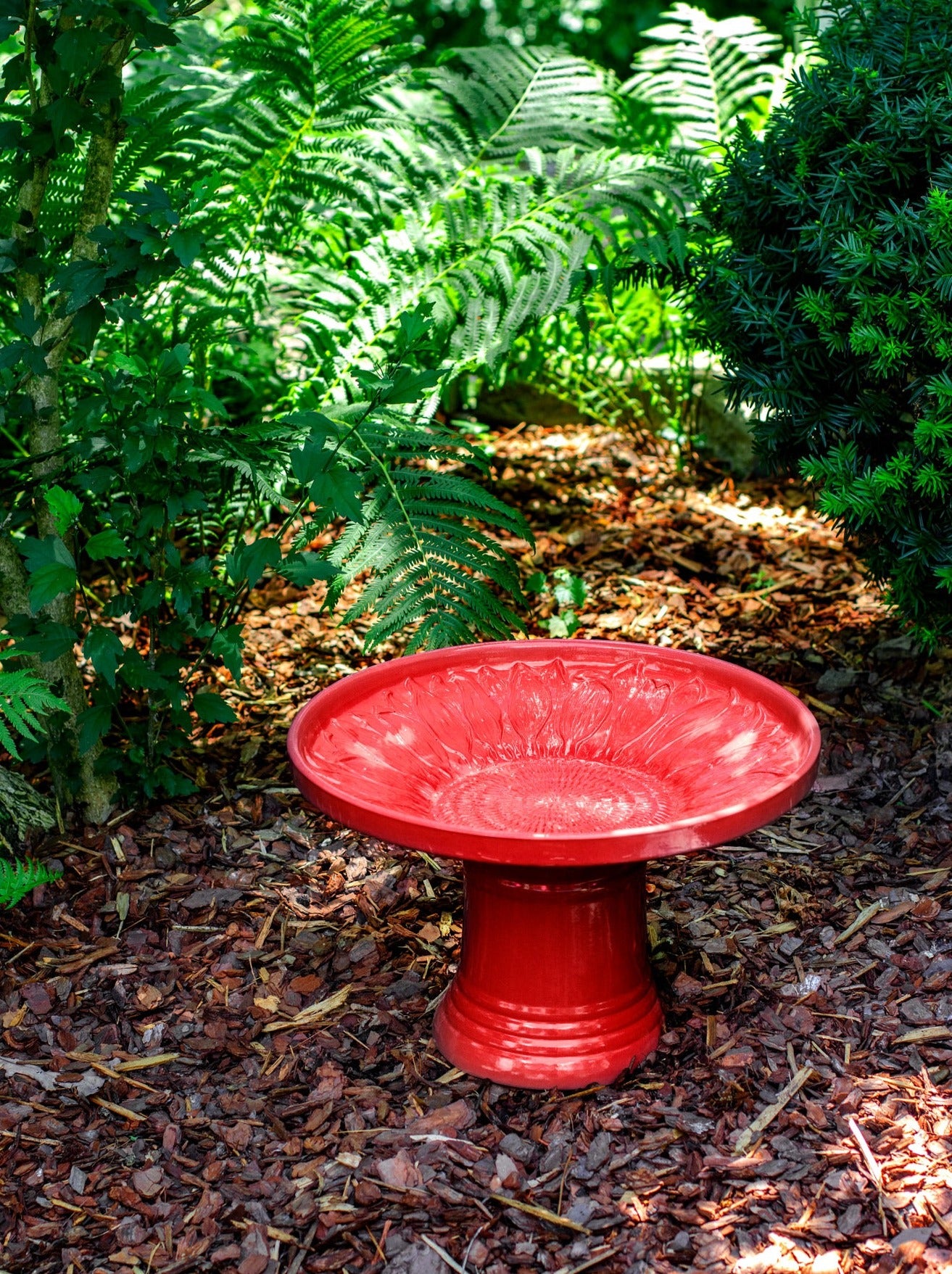 short sunflower design birdbath in red glaze in landscaped area