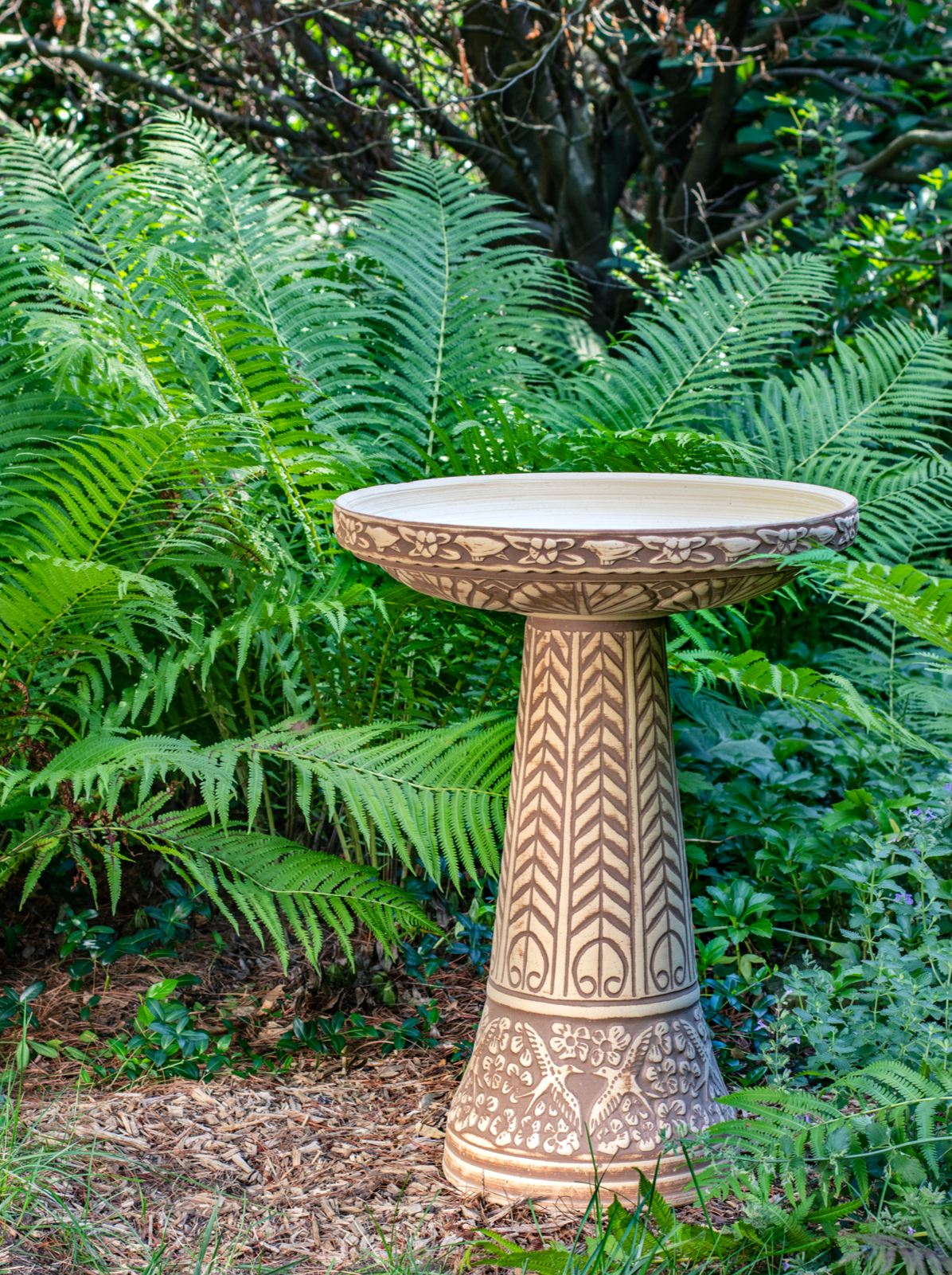 ceramic brown stained clay birdbath set with birds flowers and a chevron design in a landscaped garden setting