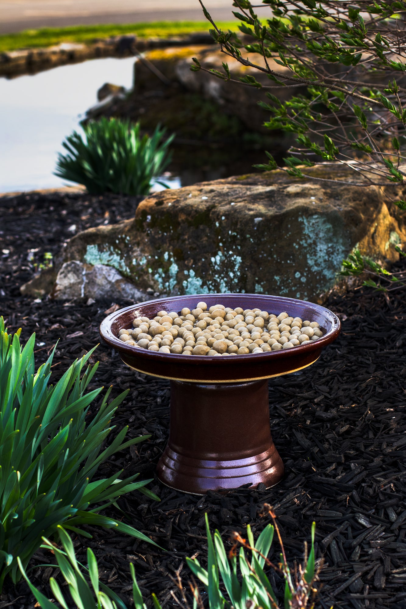 Ceramic shallow saucer with clay stones in a garden setting near a water feature