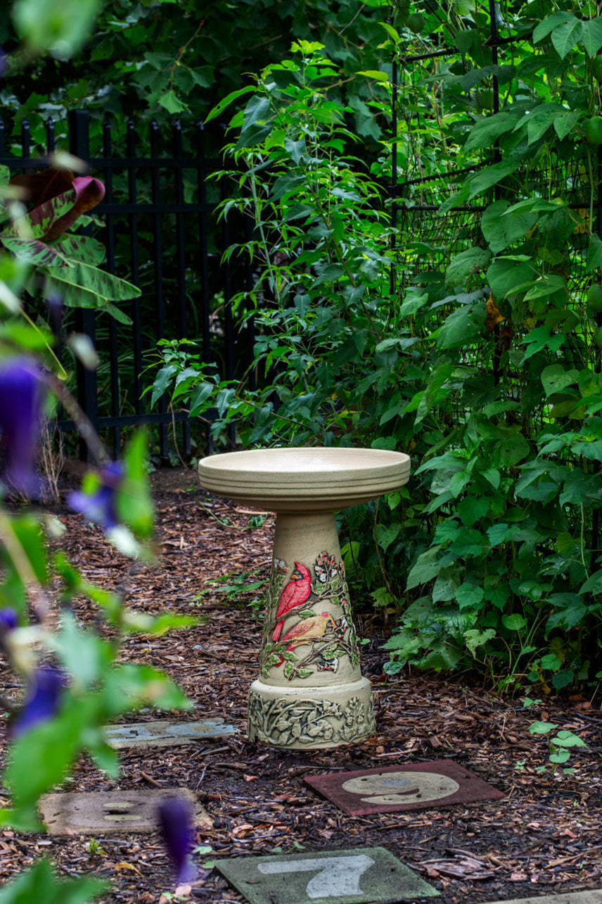 Decorative cardinal bird bath in a garden setting with greenery and flowers.