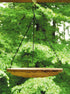 A beige, hanging nest birdbath feeder made of clay, suspended by chains against a backdrop of green foliage.