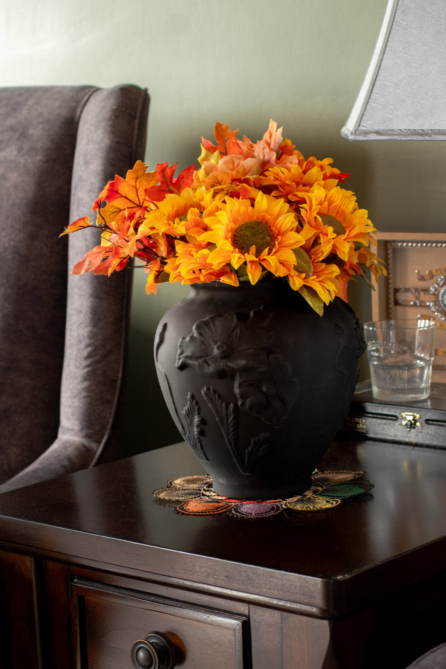 Decorative vase with autumn-themed flowers on a side table.