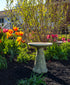 ceramic birdbath set set in a flower bed filled with brightly colored flowers and large bush