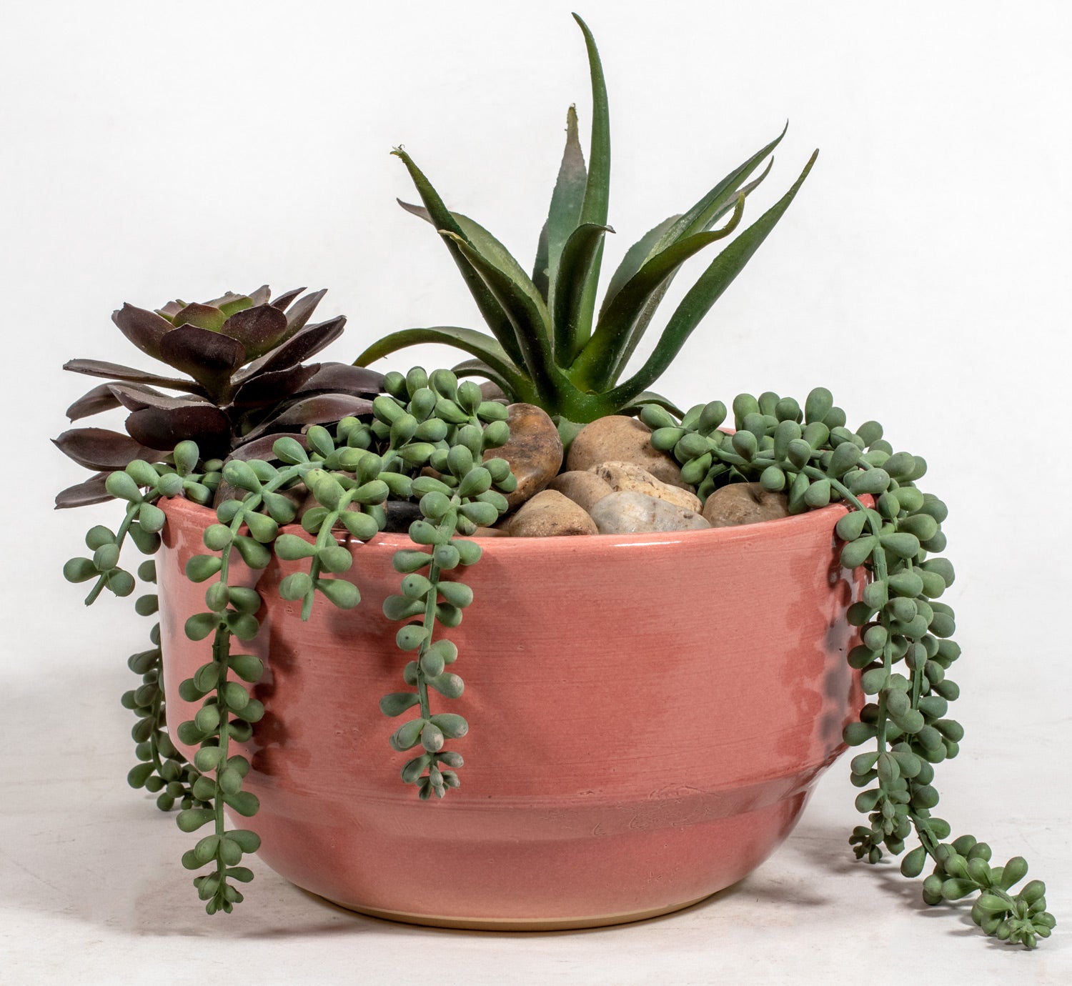small pink bowl shaped ceramic planter with string of pearl plants and succulents
