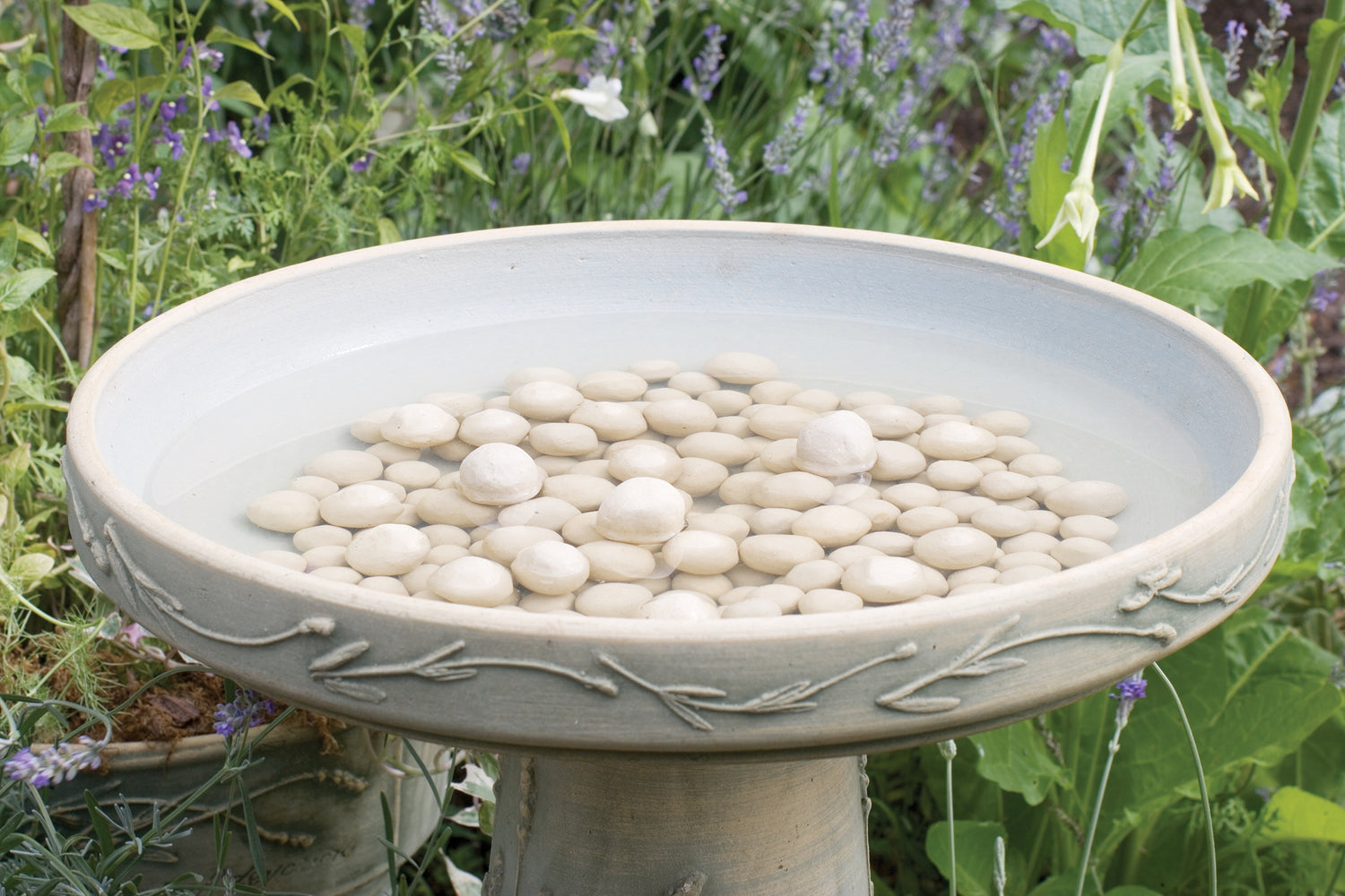 small ceramic clay balls inside a birdbath top filled with water in a garden setting