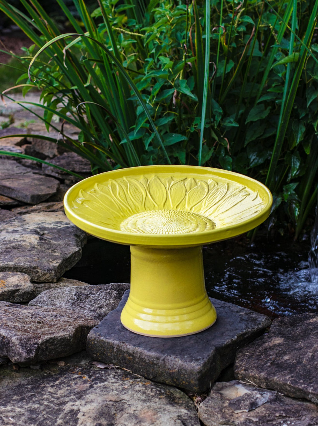 short sunflower design birdbath in yellow glaze in landscaped area