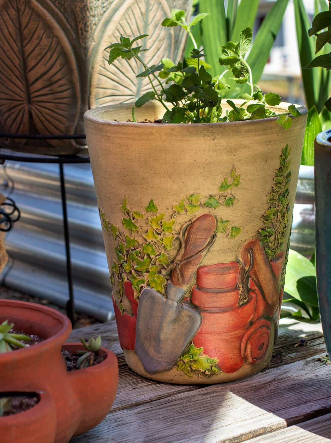 Tall fluted ceramic planter with hand painted gardening tools and terra cotta pots 