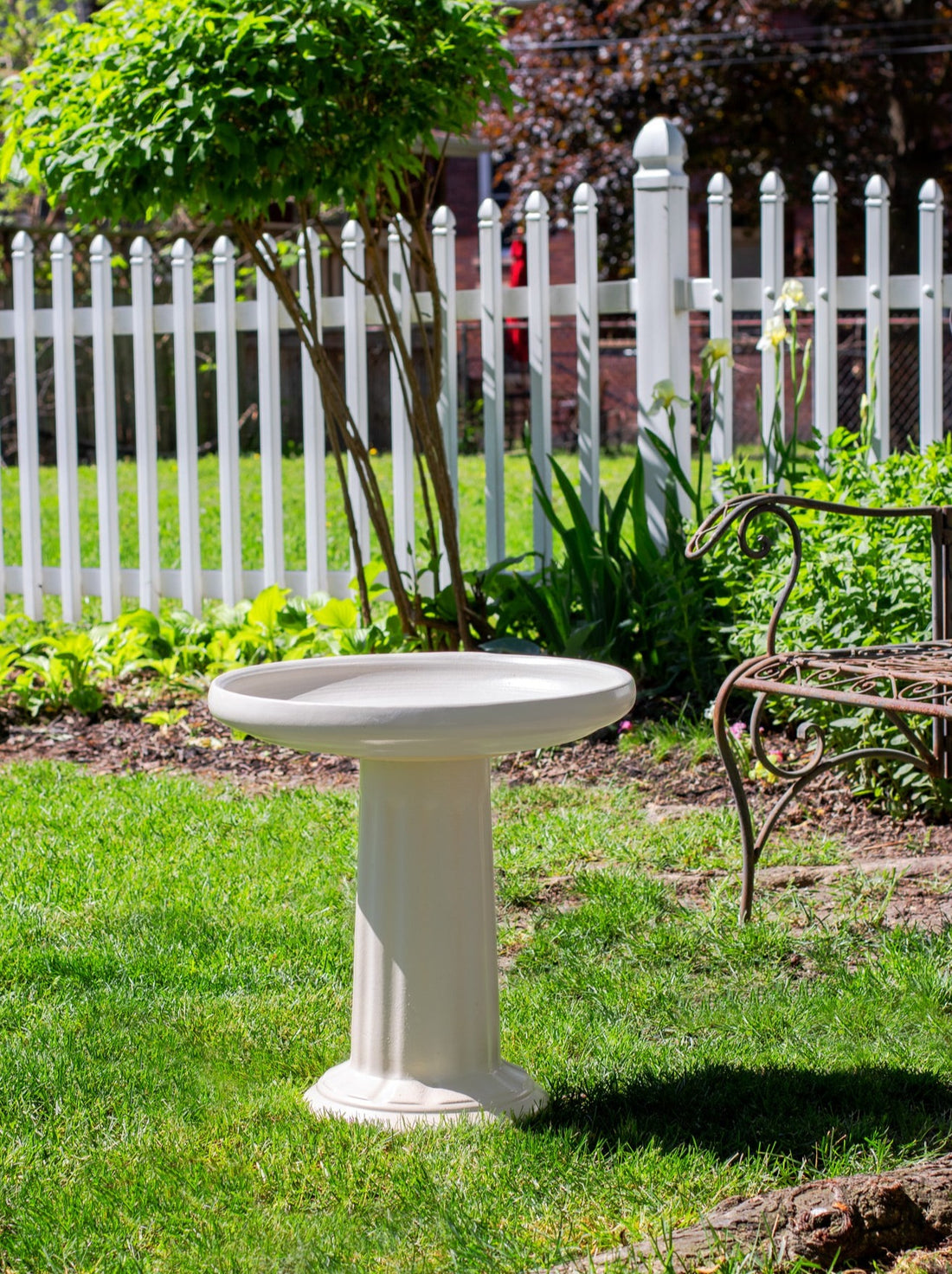 ceramic white birdbath with column design in a landscaped garden setting