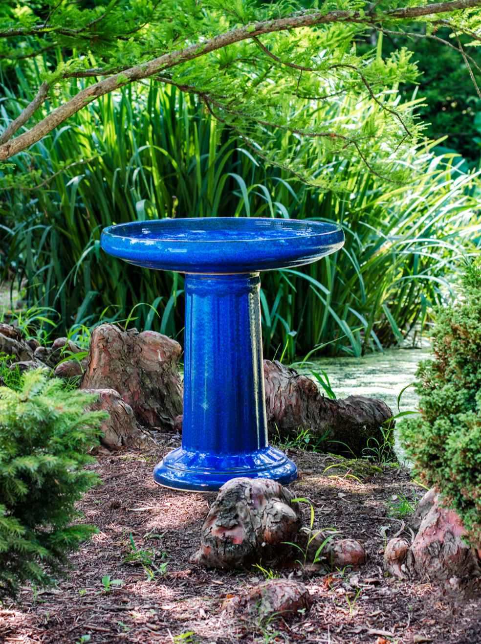 Ceramic blue birdbath set with modern clean column design in a landscaped garden setting