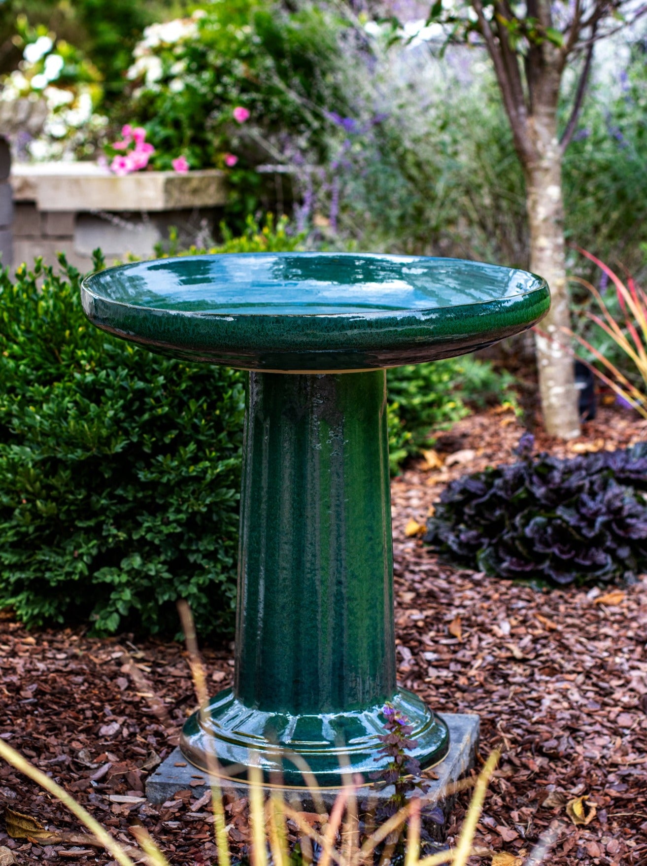 ceramic green birdbath with column design in a landscaped garden setting