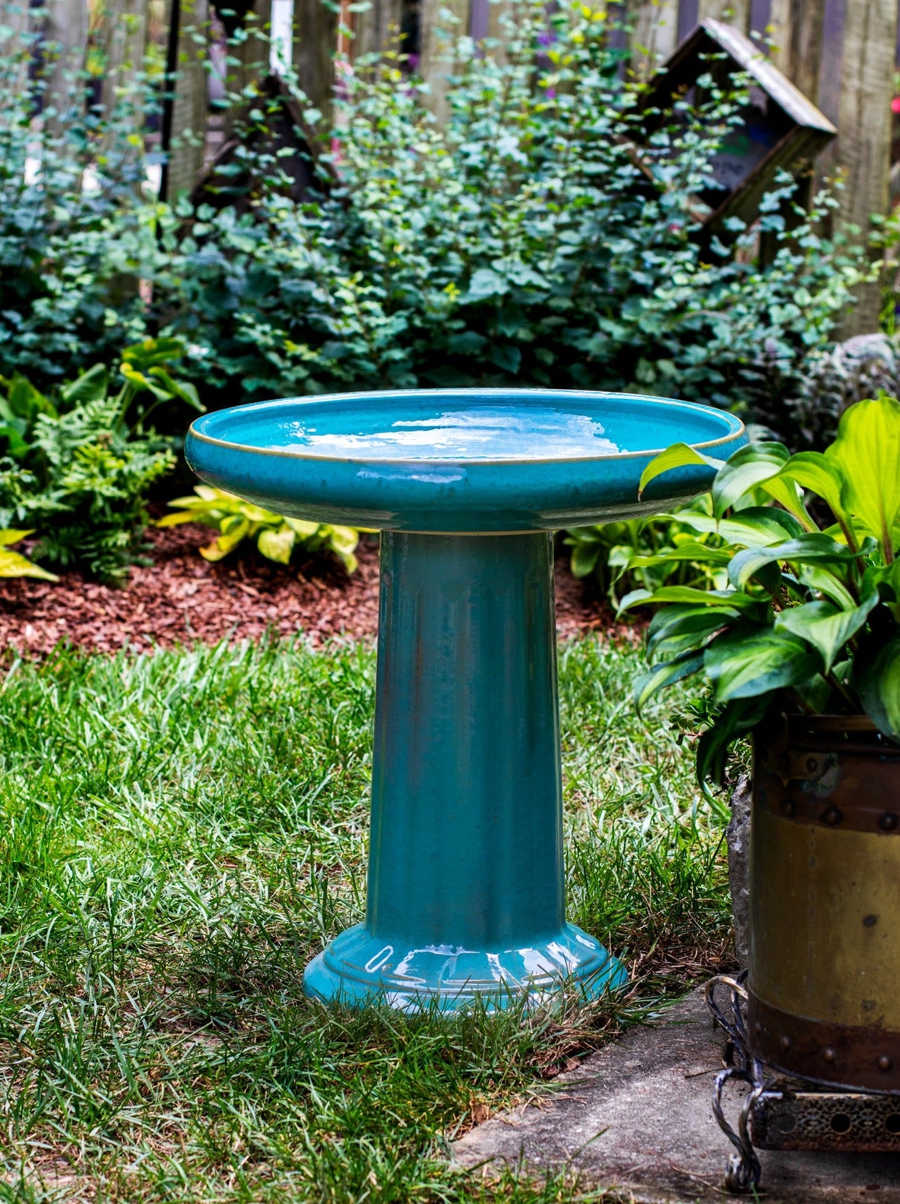 ceramic turquoise birdbath with column design in a landscaped garden setting