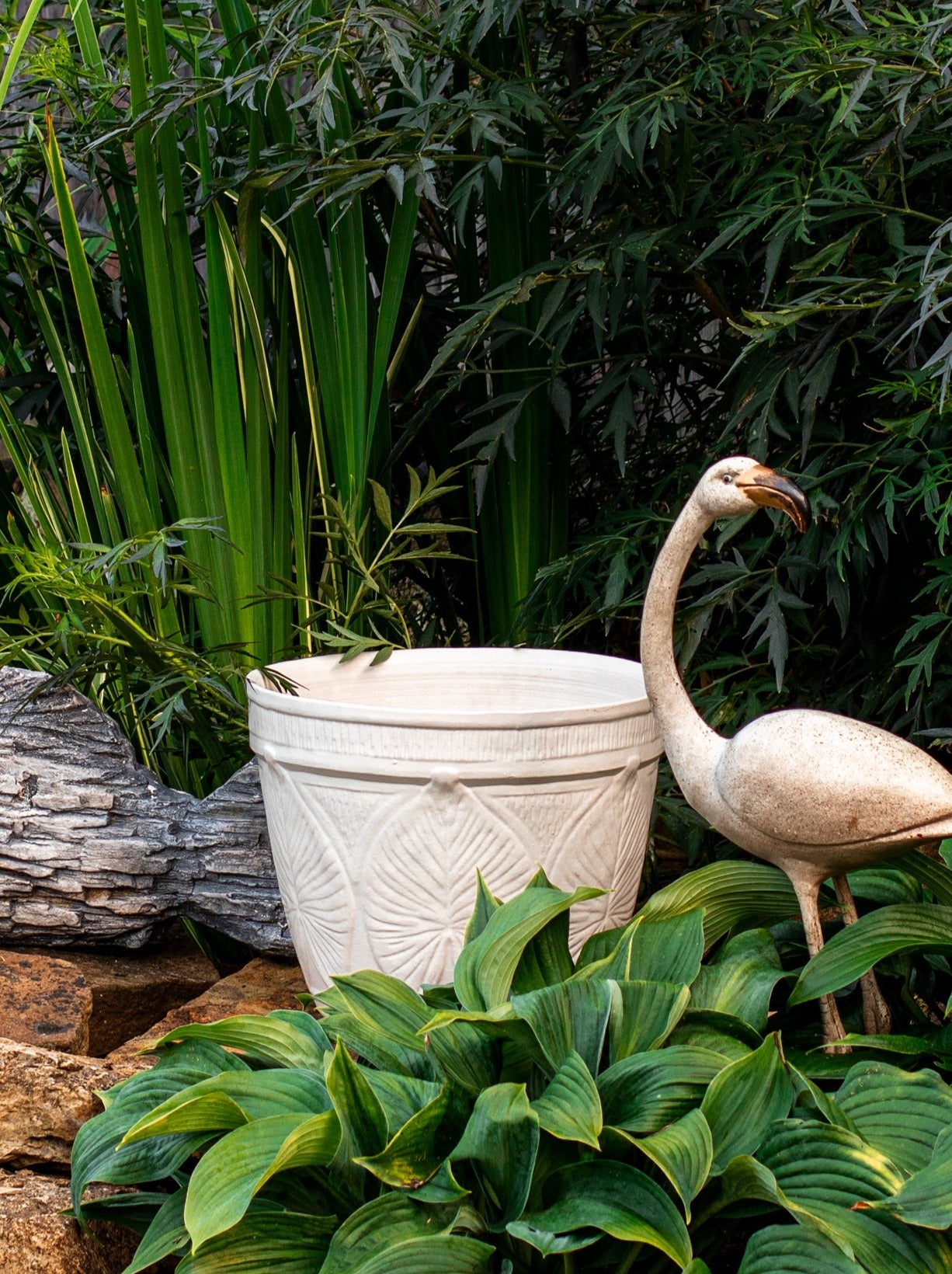 Large outdoor patio planter in white glaze with leaf design surrounded by plants and fake flamingo