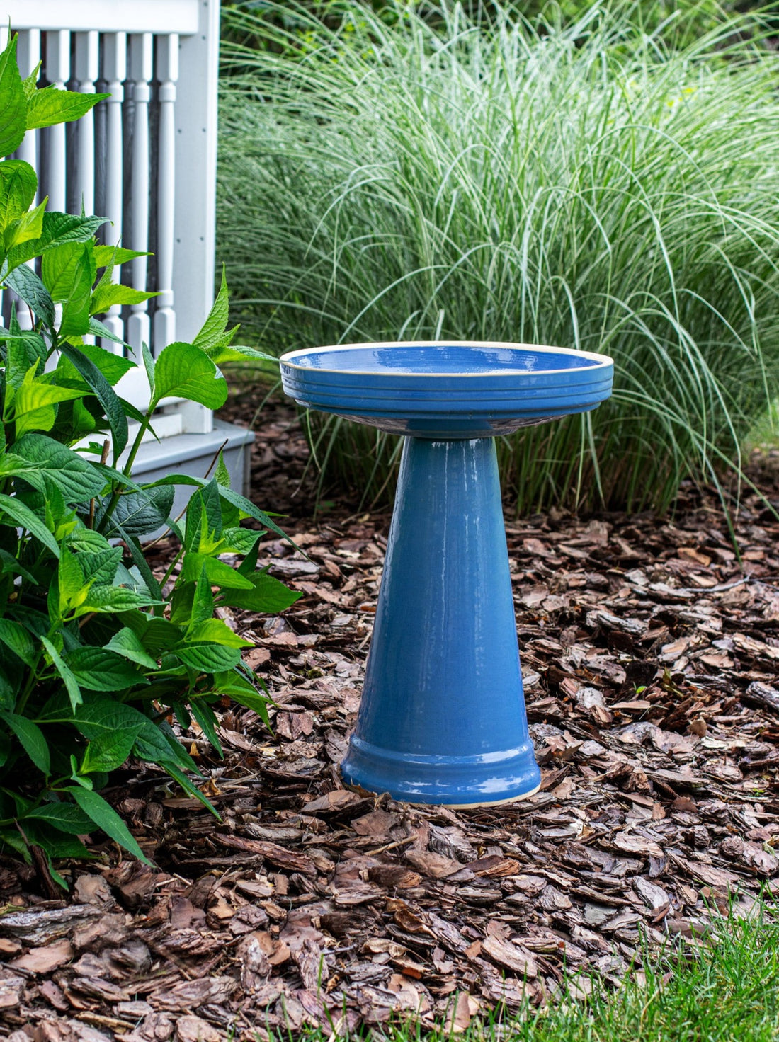ceramic light blue birdbath with simple modern smooth design in a landscaped garden setting