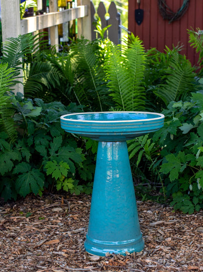 ceramic turquoise birdbath with simple modern smooth design in a landscaped garden setting