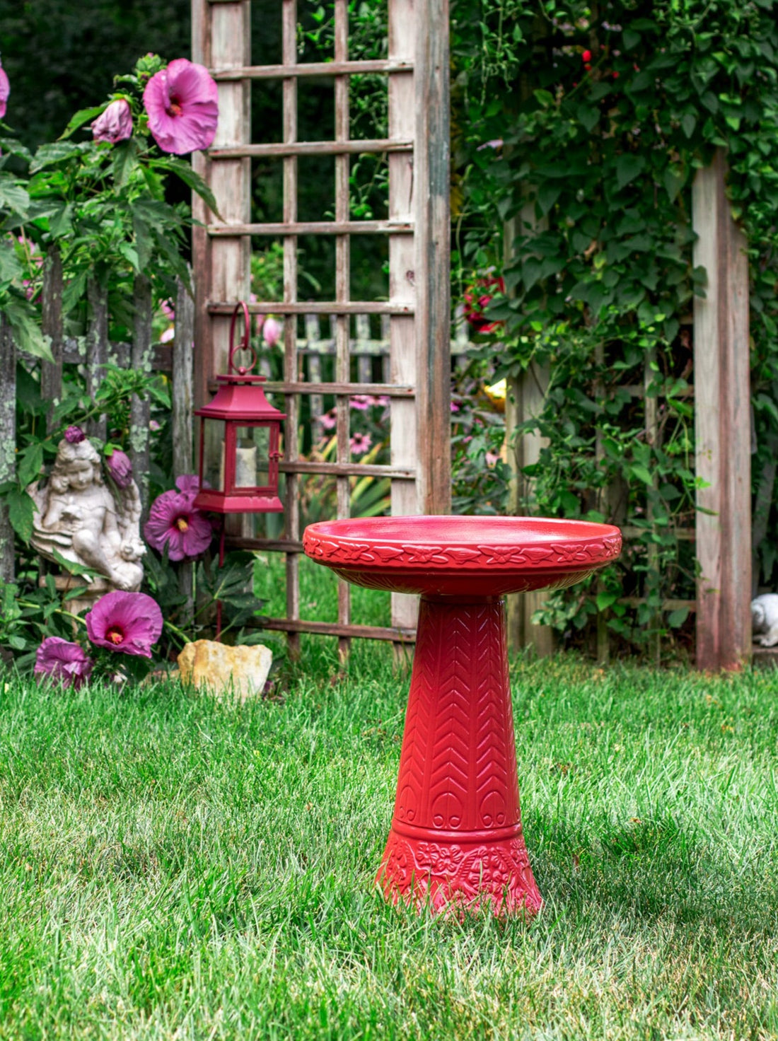 ceramic red glazed birdbath set with birds flowers and a chevron design in a landscaped garden setting