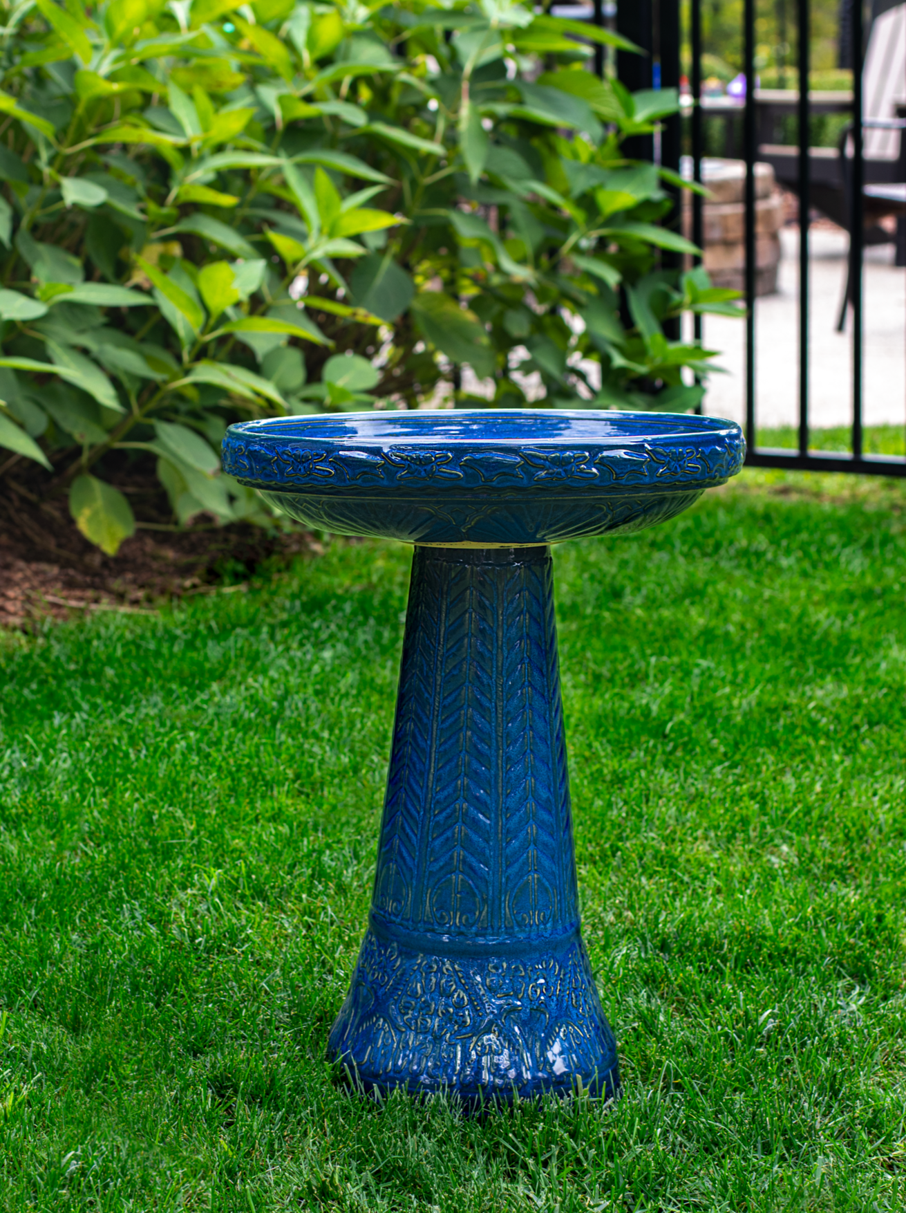 ceramic blue birdbath with birds and flowers design in a landscaped garden setting