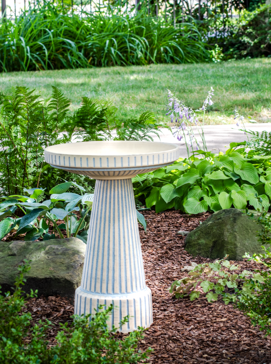 ceramic clay light blue stained birdbath set with stripped design in a landscaped garden setting