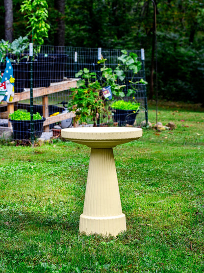ceramic birdbath set in tan color in a landscaped garden setting