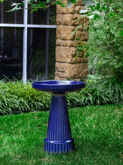 ceramic blue birdbath with stripped design in a landscaped garden setting