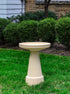 ceramic birdbath set in white striped tan color in a landscaped garden setting