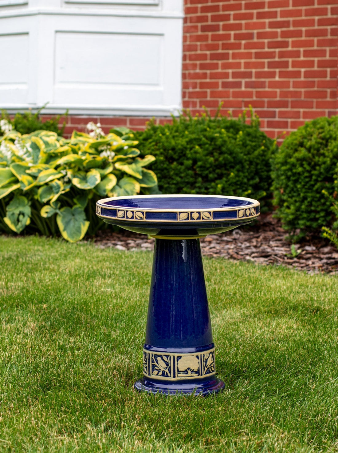 Ceramic Blue birdbath set with tan tree leaf and bird design in a landscaped garden area